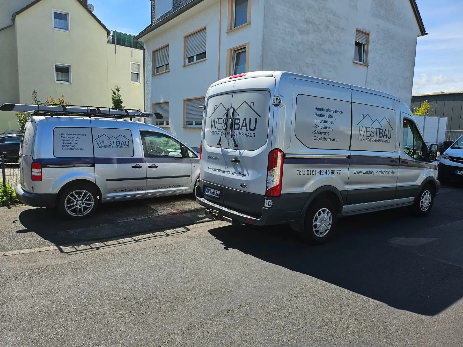 Zwei beschriftete Fahrzeuge von Westbau vor einem Wohnhaus im Ahrtal